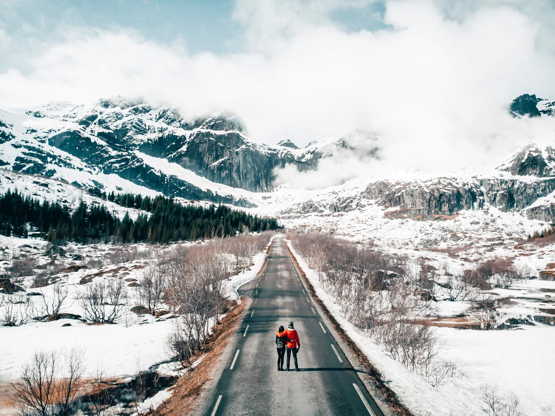 A young travelling couple on a long icy road in Norway seek new undiscovered holiday destinations