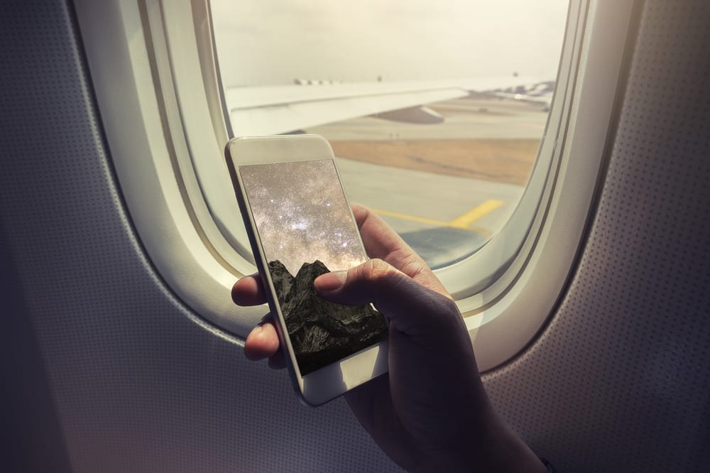 person holding a smartphone in front of a plane window