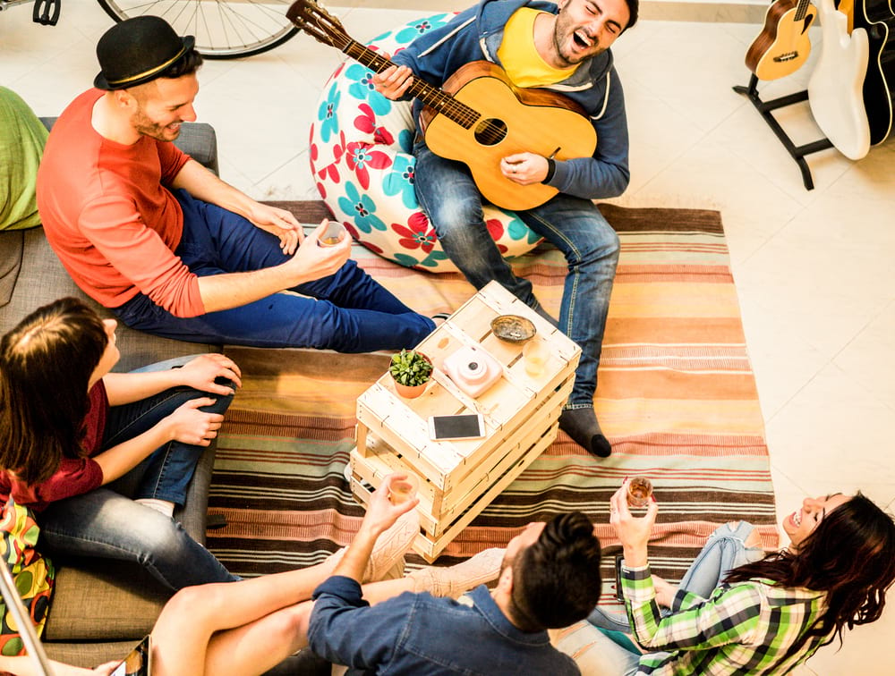 Group of backpackers in a hostel common room listening to a guy playing the guitar.