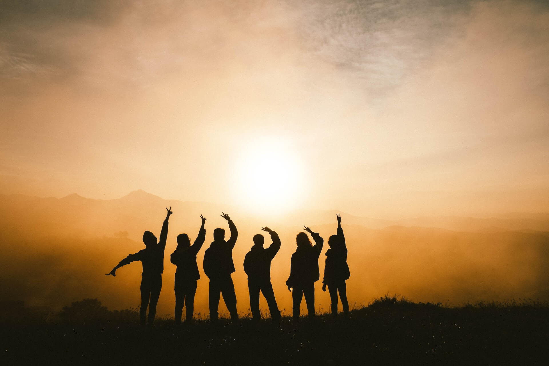 A group of travellers who met while staying in a hostel for the first time silhouetted against a sunset