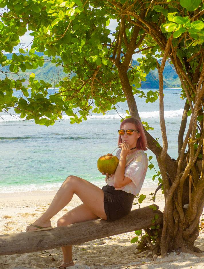 Elina drinking a coconut on a beach
