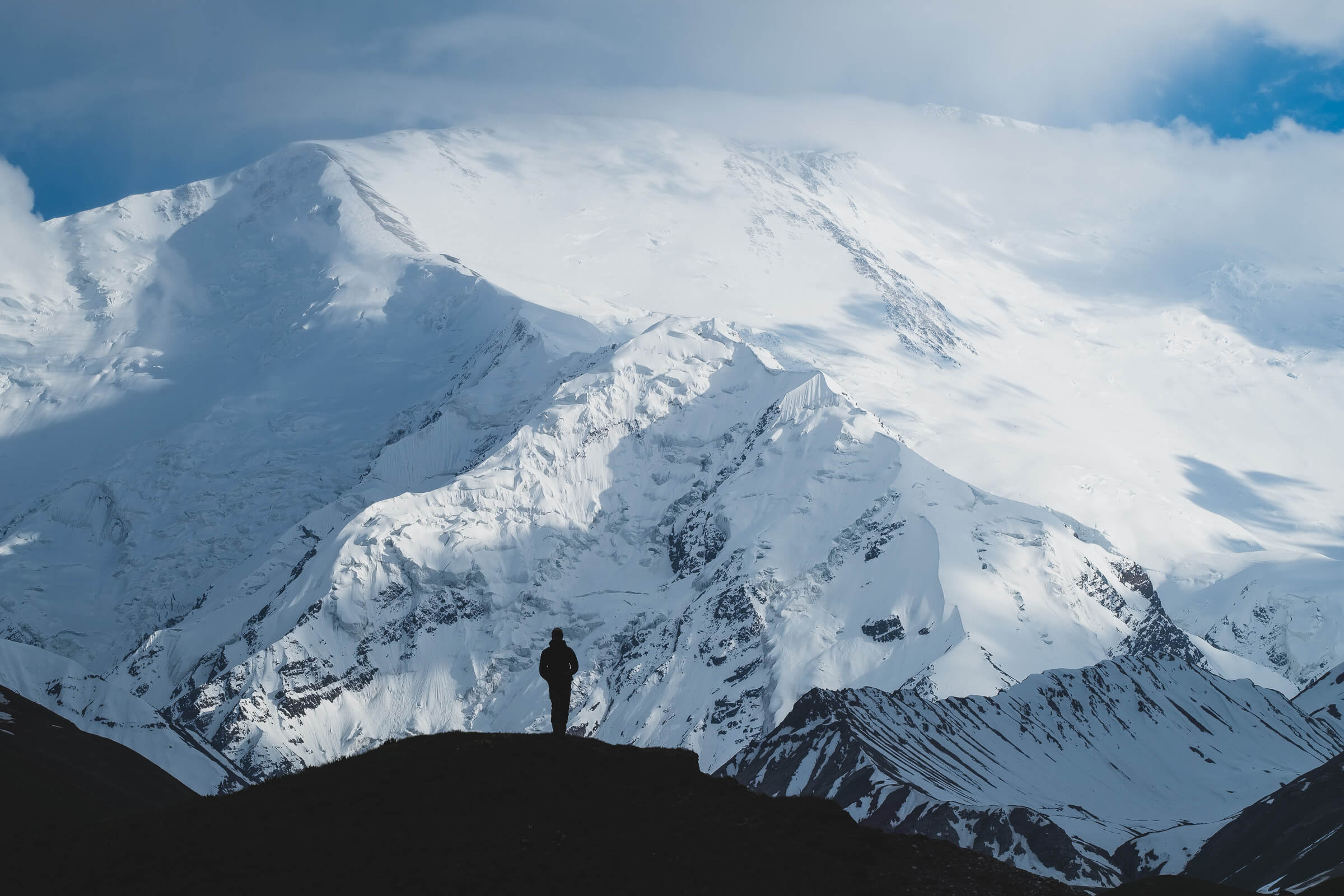 hiker standing on top of a hill with a huge white mountain in the background