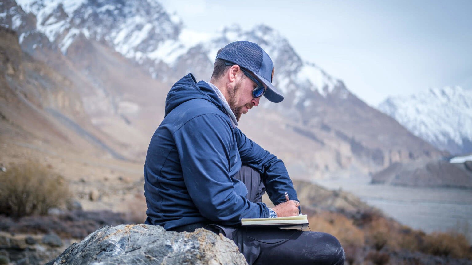 man journaling while sitting on a rocks in the mountains of pakistan