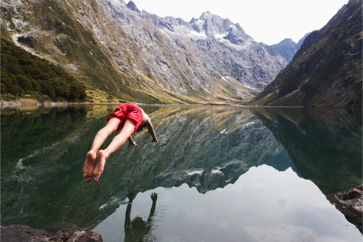 A man in red board shorts dives into cold Milford Sounds water. 