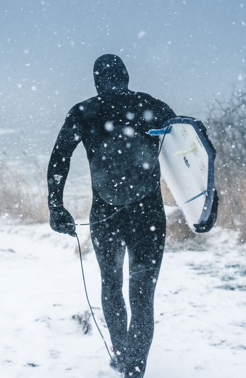 A man heading to the beach in a snowstorm wearing a thermal wetsuit