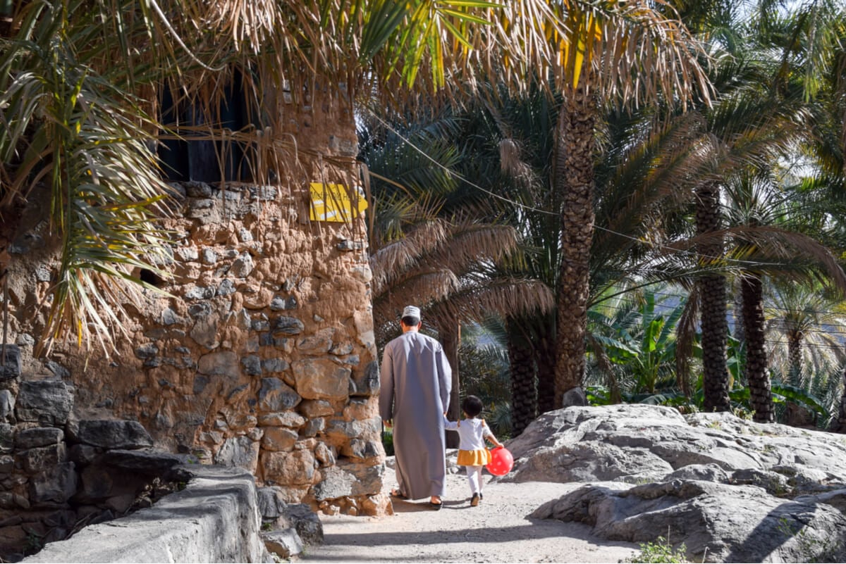 a man walking with his daughter under date trees in one of the most beautiful places in oman