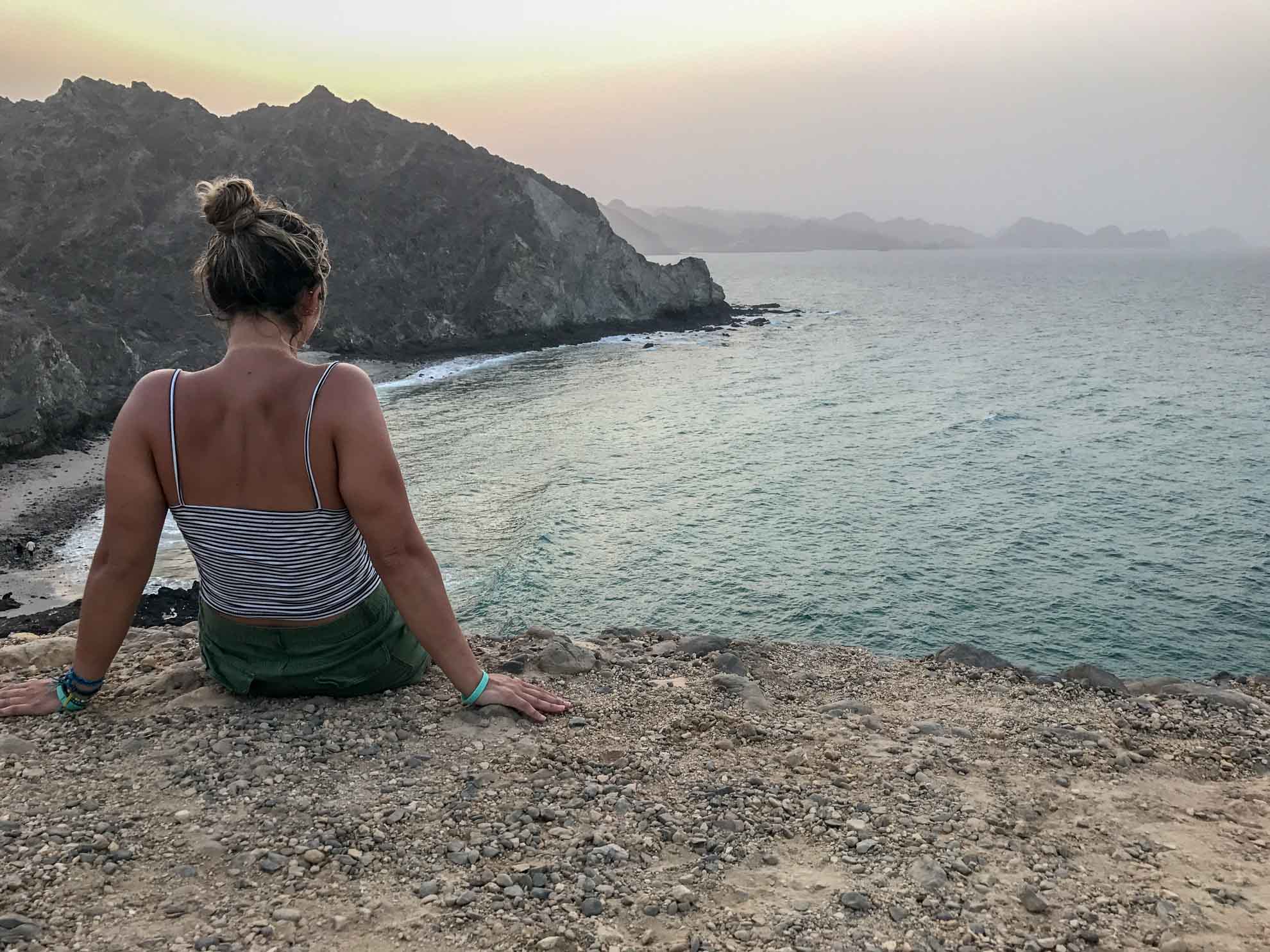 girl looking out at ocean and mountain view while visiting oman