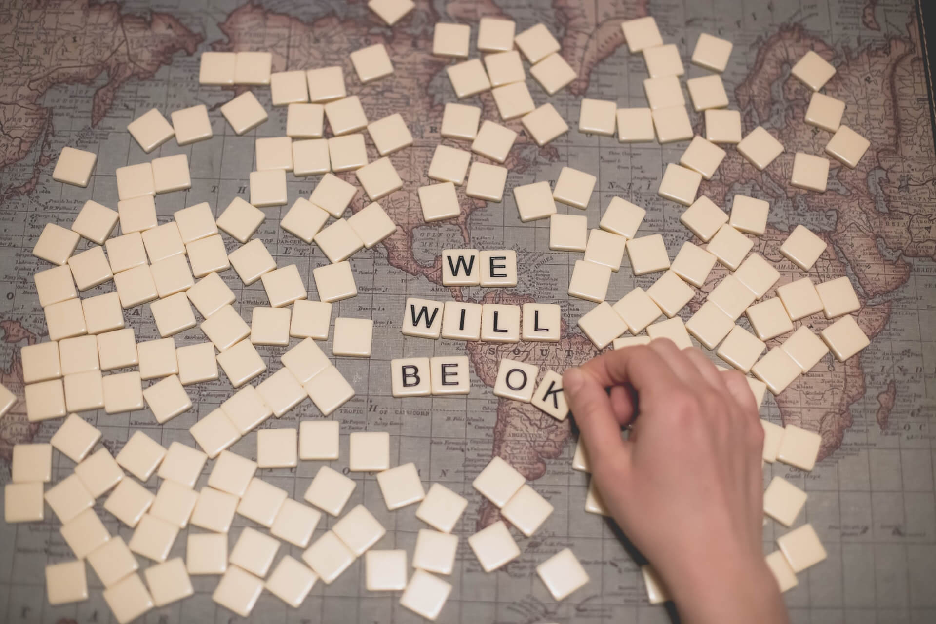 Placing out the words 'We Will be Ok' with scrabble tiles on a world map