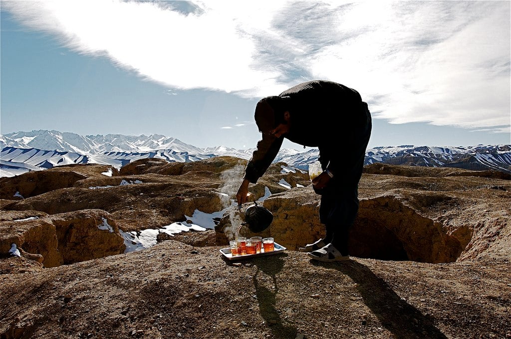 A man pours several cups of tea within snow capped mountains in Afghanistan.