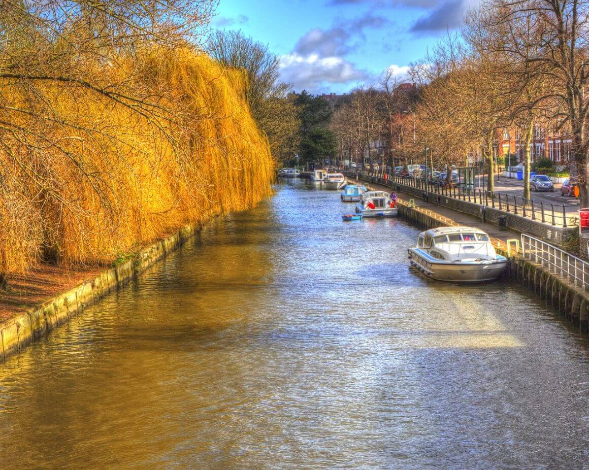 calm river with several colorful boats docked along the bank in Norwich, England