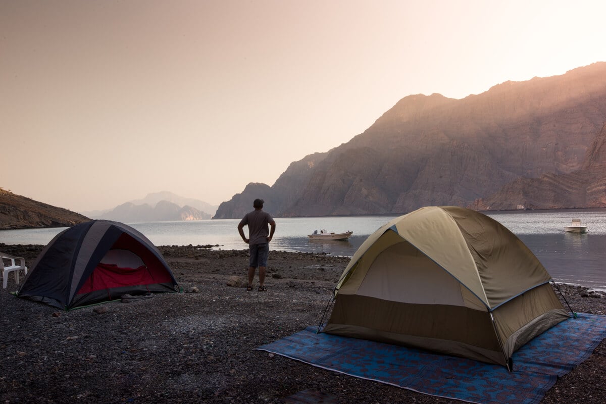 man standing in between two tents watching an orange sunset while visiting oman