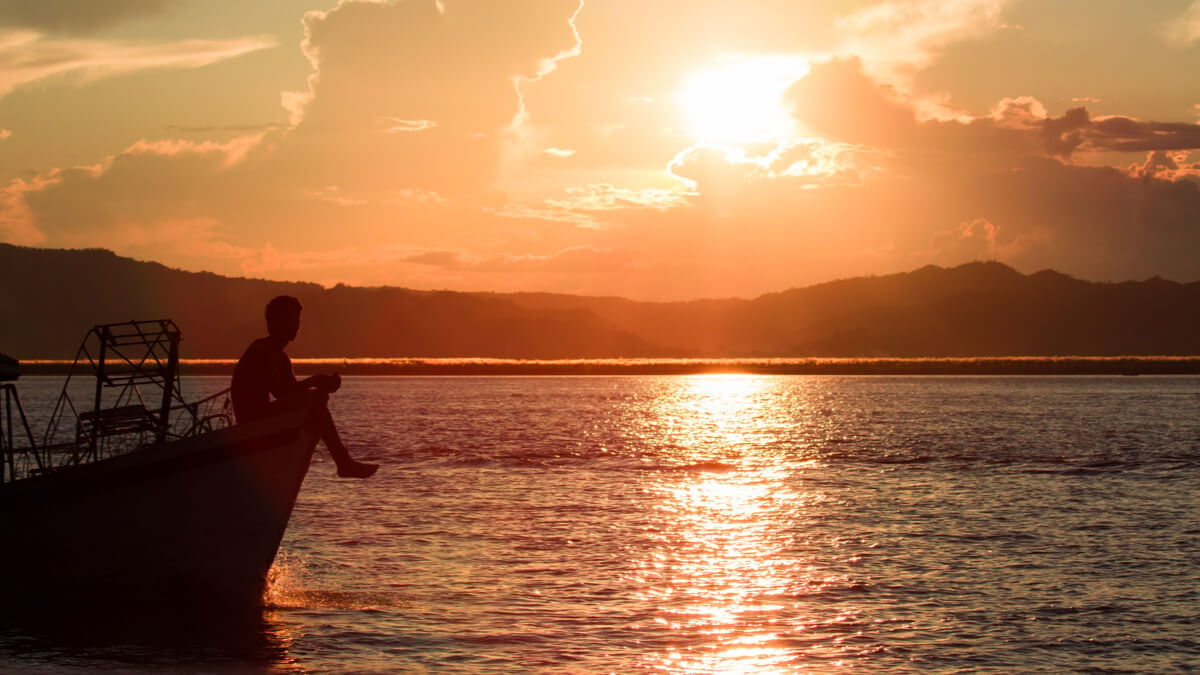 A man sits on a boat at sunset in the Caribbean Islands. 