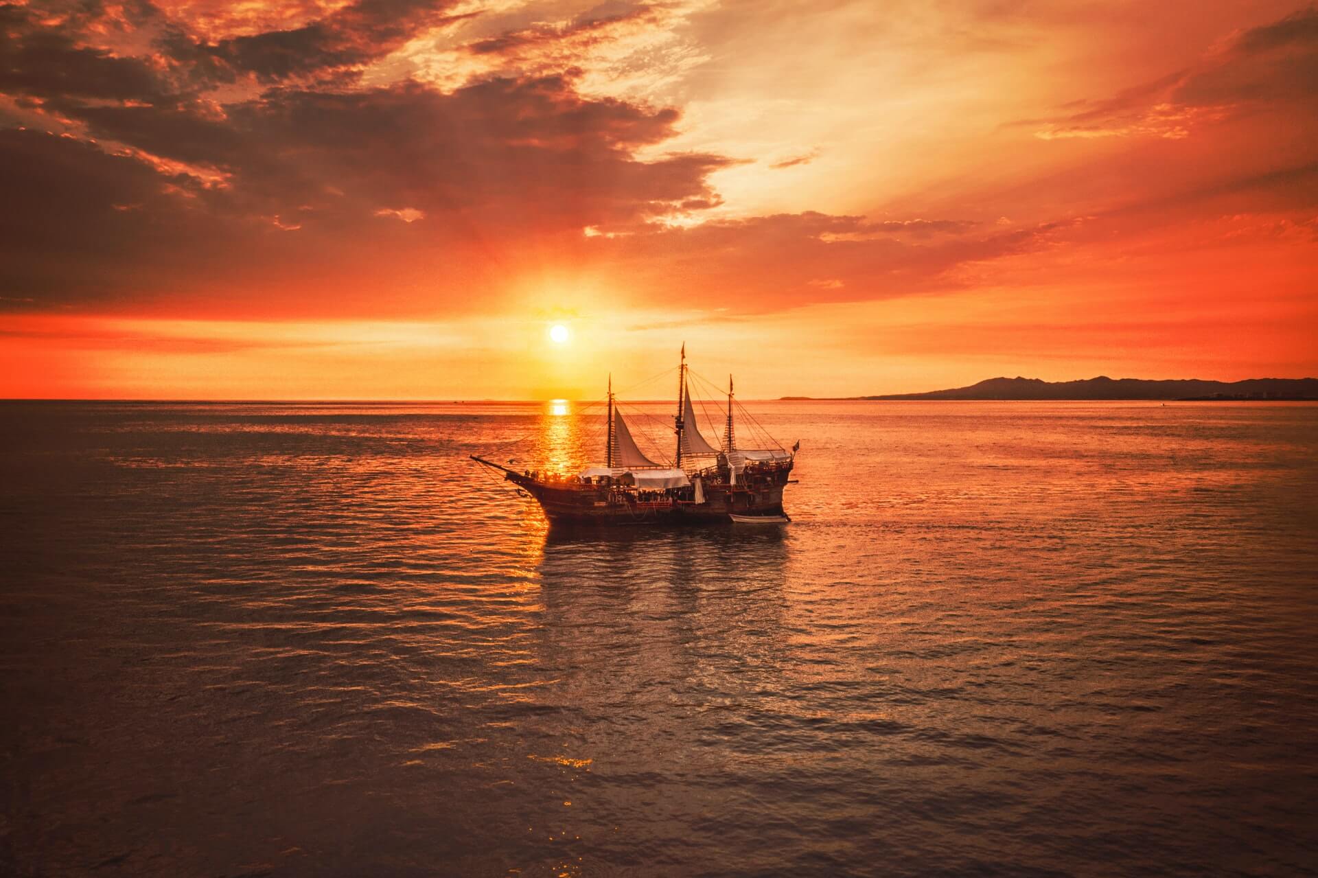 A sailboat mid-cruise on a sunset lake.