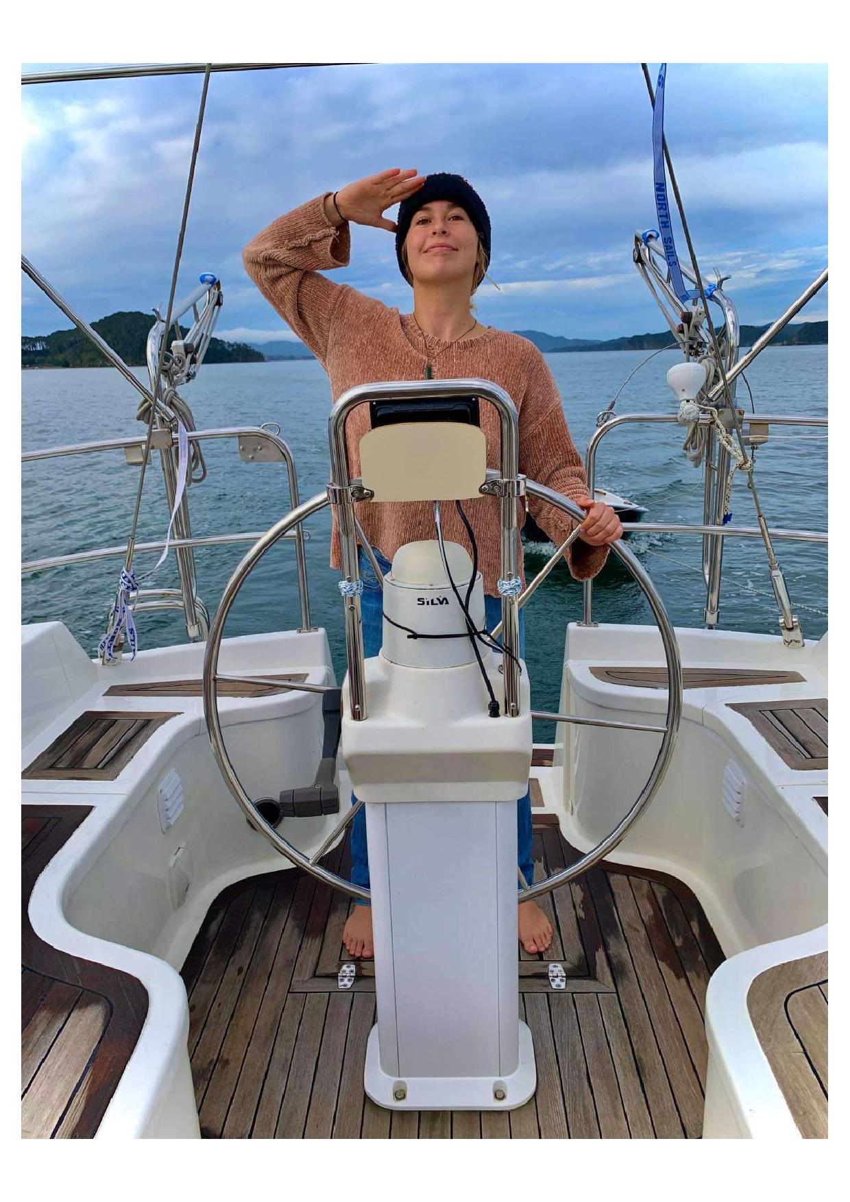 A girl stands at the helm of a sailboat looking at the horizon. 