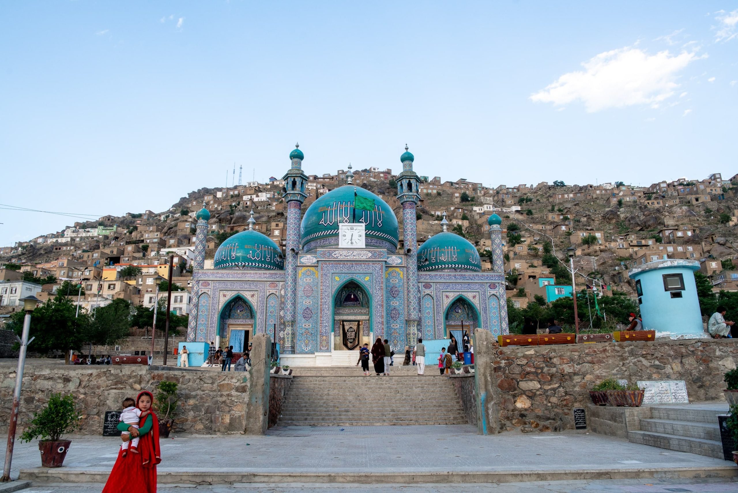 A blue mosque with people around it in Kabul. 