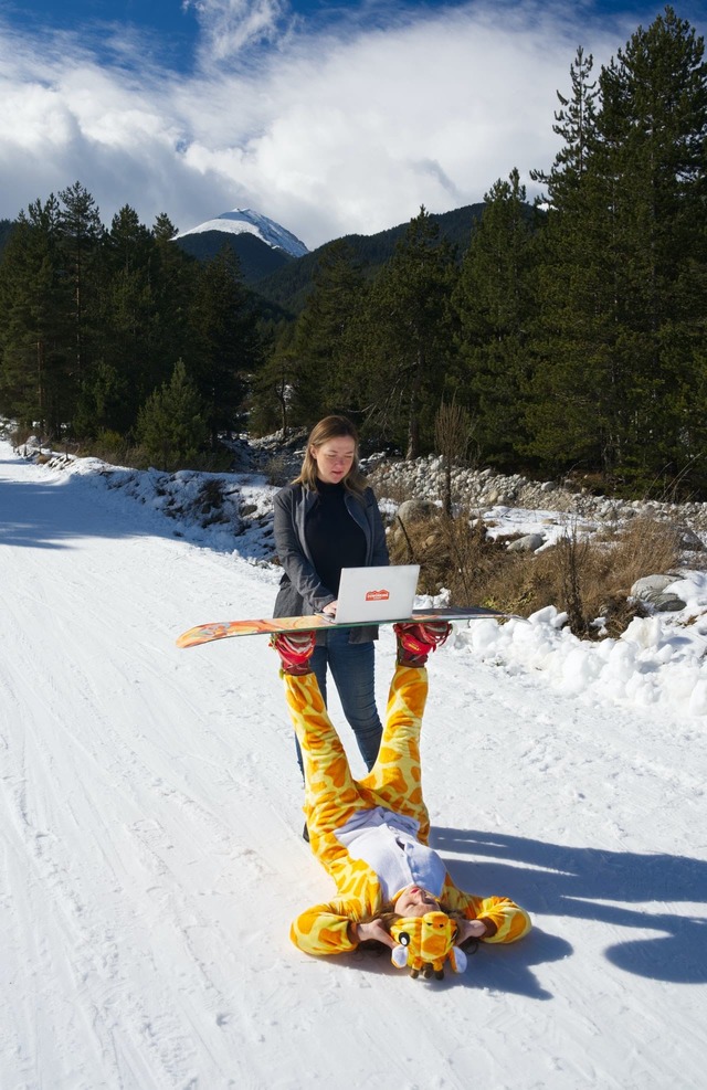 digital nomad working on a laptop positioned on top of a snowboard held up by another digital nomad in a tiger onesie