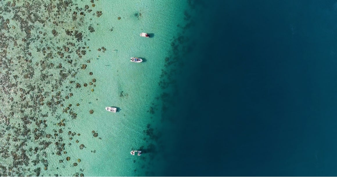 French Polynesia from the air - the light blue of the shallow water contrasts with the dark blue of the deeper water. 