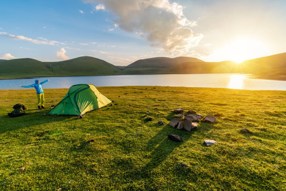 girl next to a tent and lake at sunrise