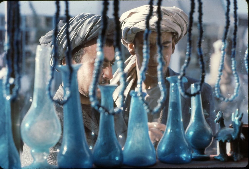 Two men look on at blue glass in a market in Afghanistan.