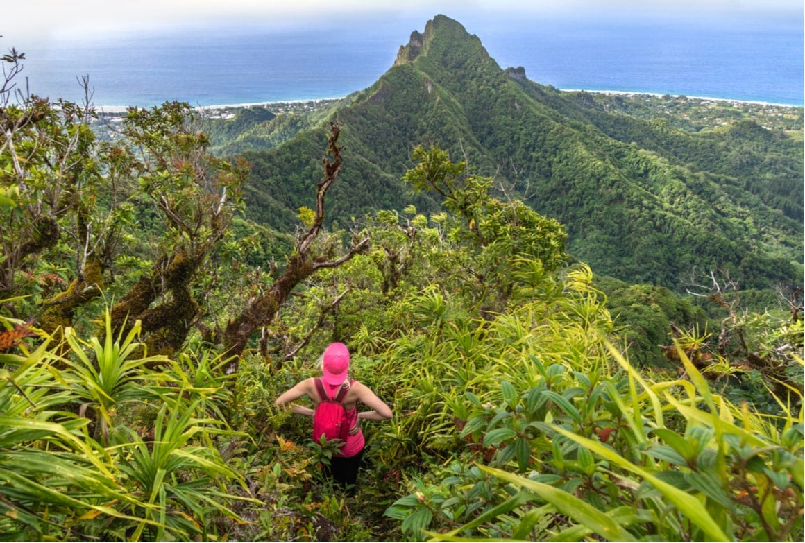 A girl in pink watches the view of Rarotonga from a hiking trail. 