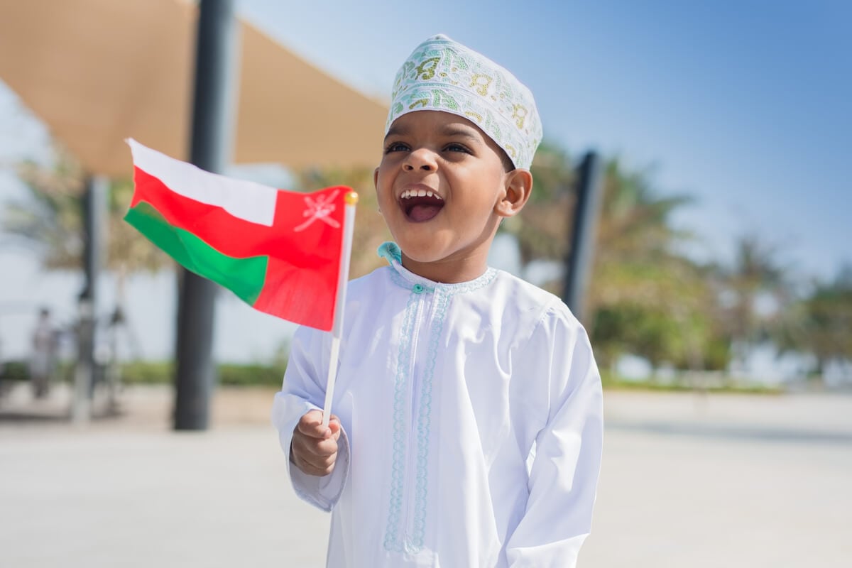 A small local boy in Oman waves an Omani flag and smiles