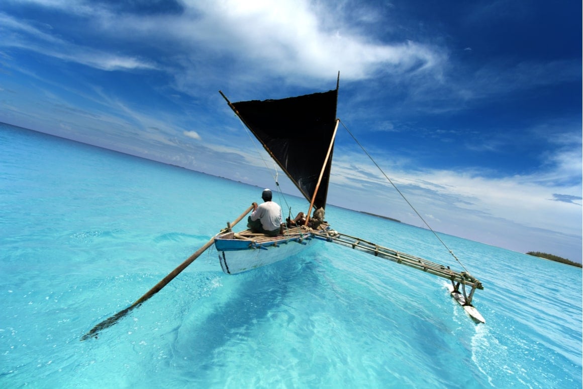 An outrigger canoe is steered through light blue water
