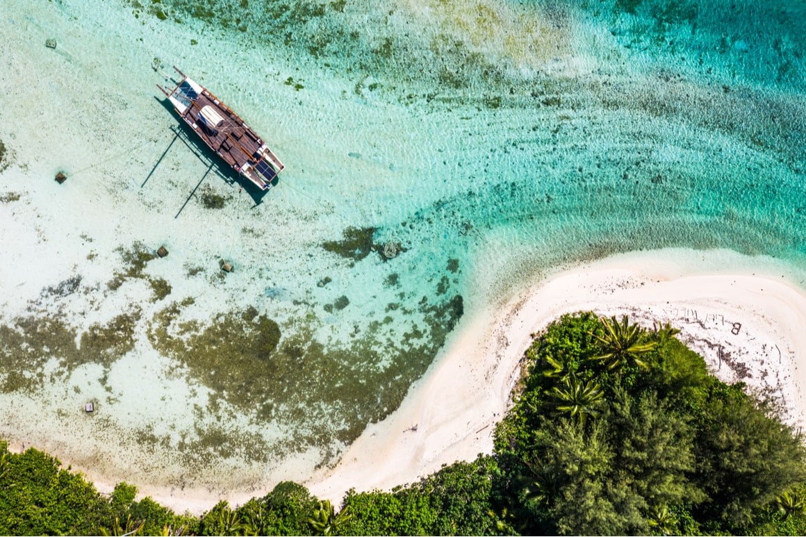 An aerial shot of a sailboat in the clear water of the Cook Islands. 