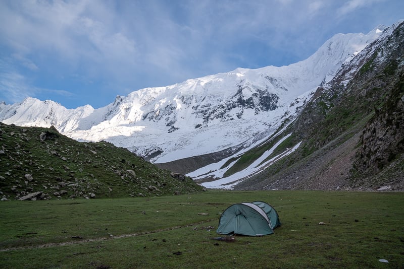 green tent in meadow beneath massive mountain backpacking in pakistan