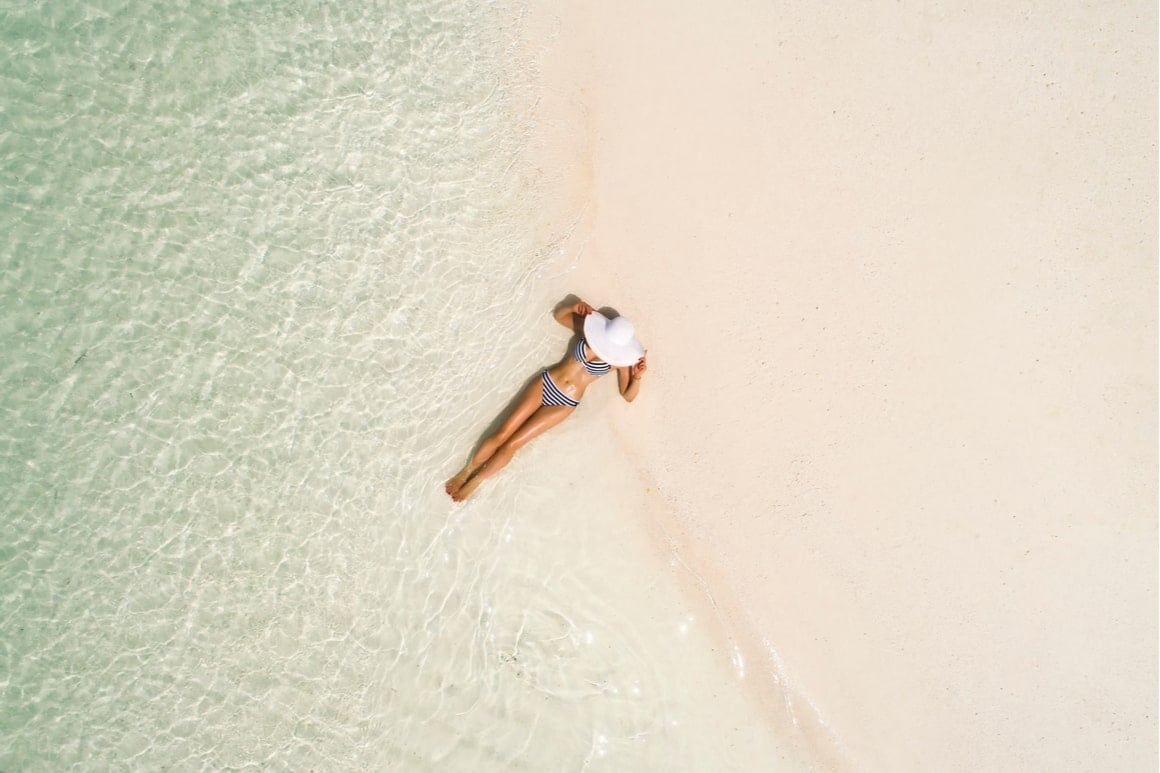 A girl lies in clear water of the Cook Islands while sunbathing. 