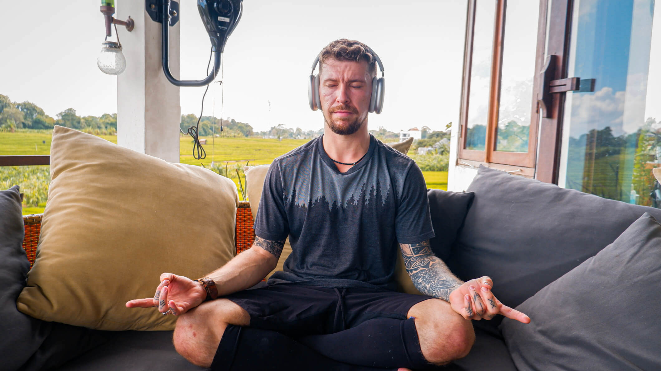 man meditating on an outdoor porch with green rice fields behind him