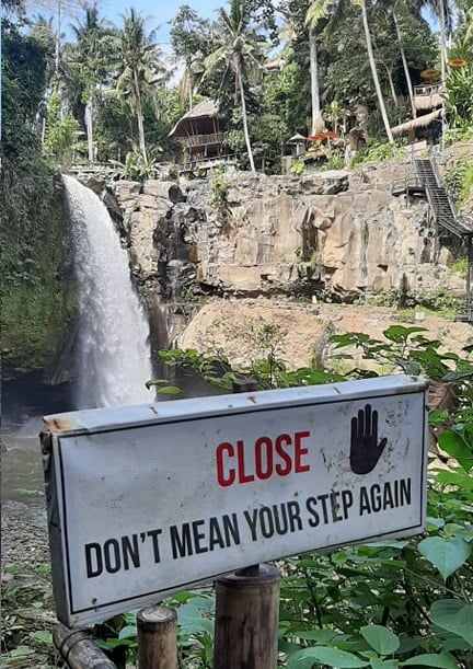 Sign at a waterfall in Bali saying "Close: don't mean your step again"