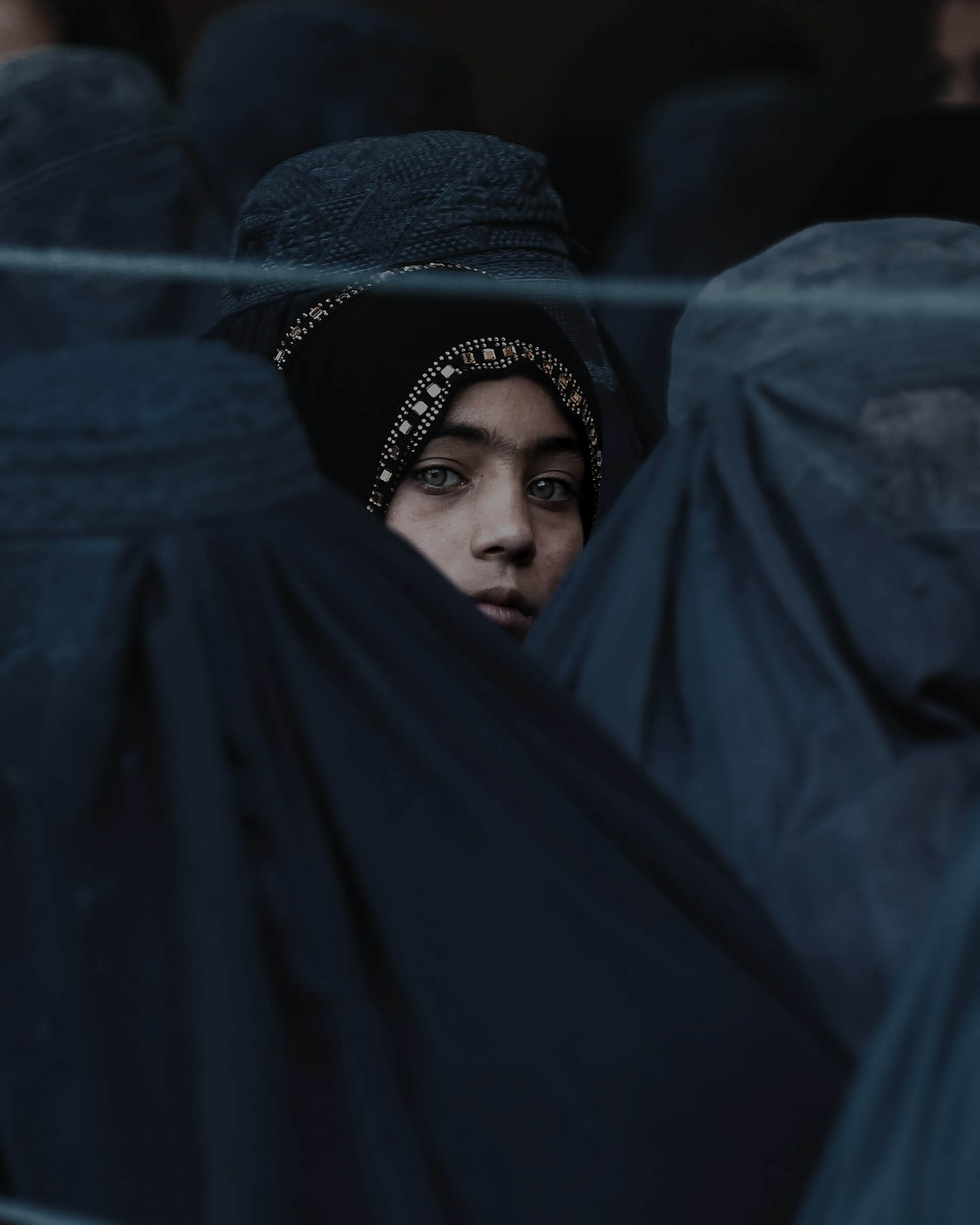 A young Afghan girl with blue eyes in a crowd of locals wearing burqas.