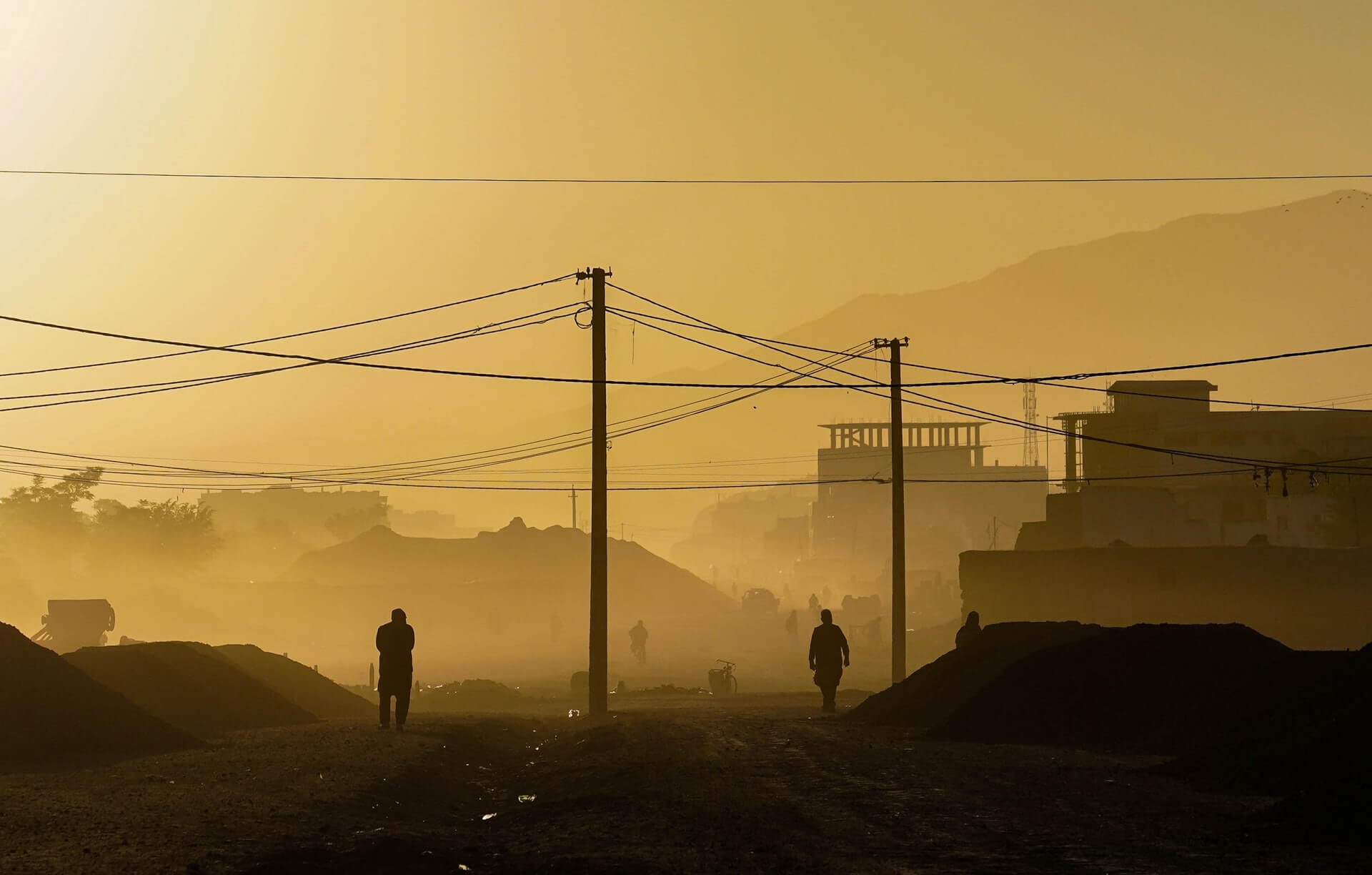 Locals walk down a dusty, desolate street in Kabul at sunrise.