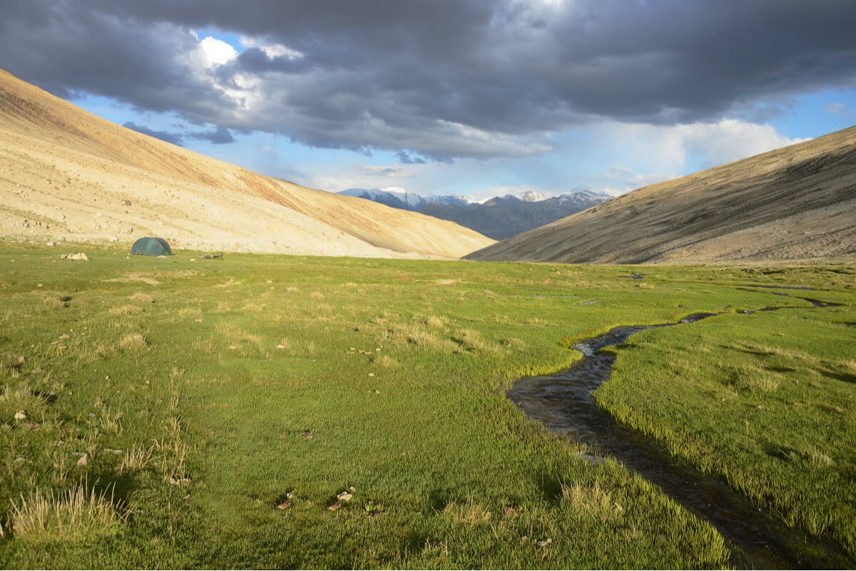 A backpacker in Afghanistan camping on a grassy flat in the Wakhan Corridor.