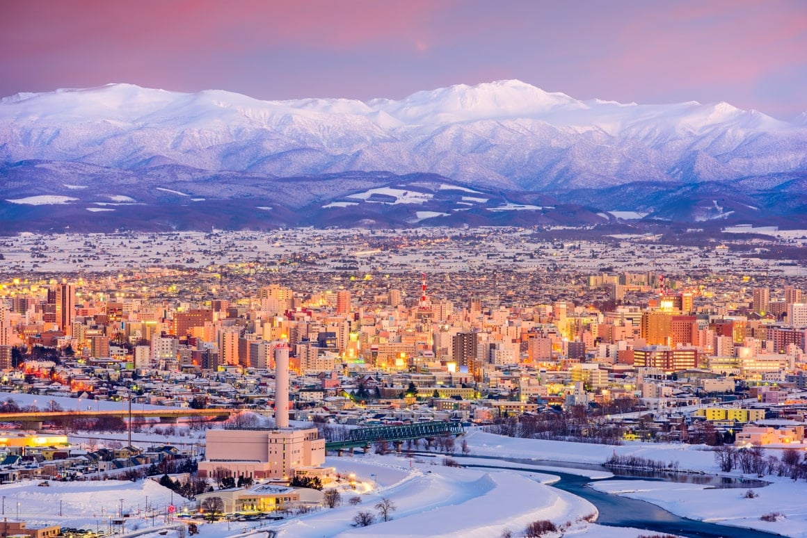 A city at sunrise in Hokkaido with snow capped mountains in the background