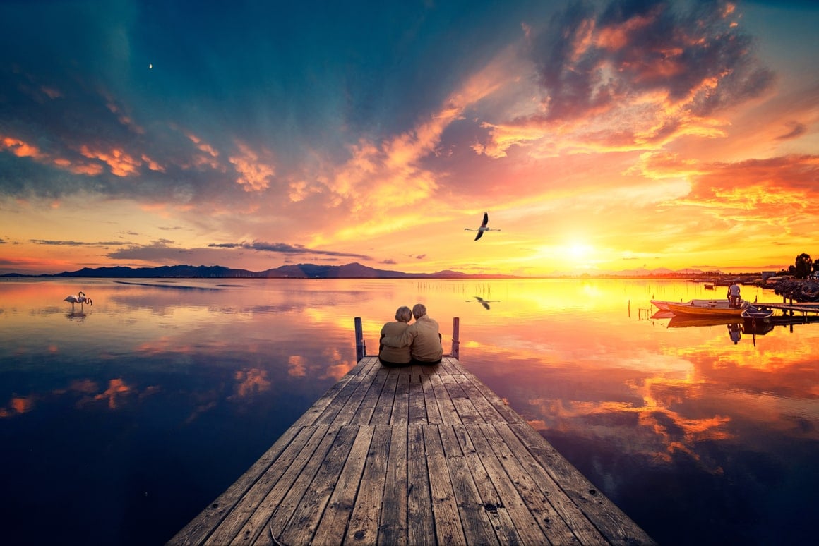 A couple sit at the end of a dock at sunset.