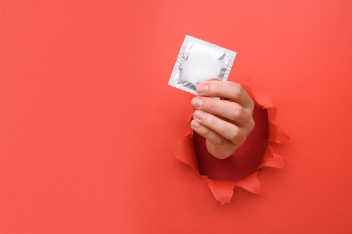 Red wall with a condom in hand