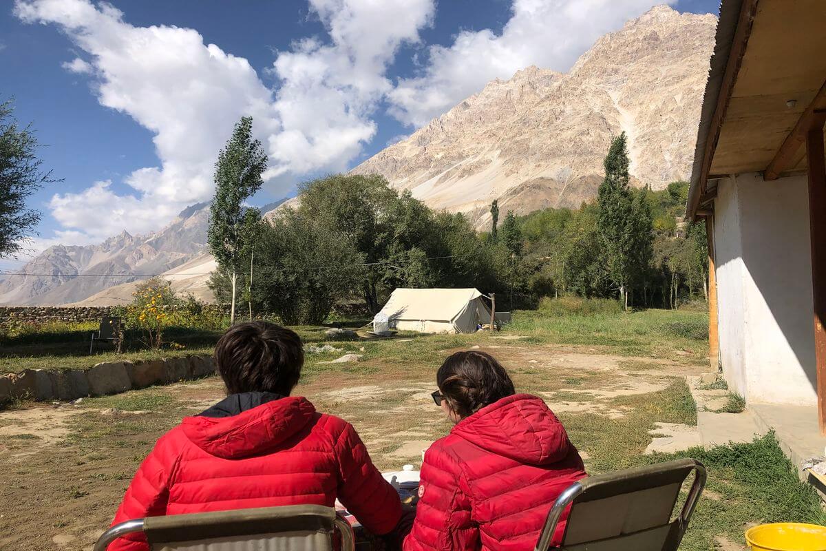 couple sitting at table in grassy yard looking out at a garden and mountains at a homestay