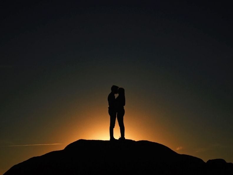 couple standing on mountain in an epic sunset of orange and black