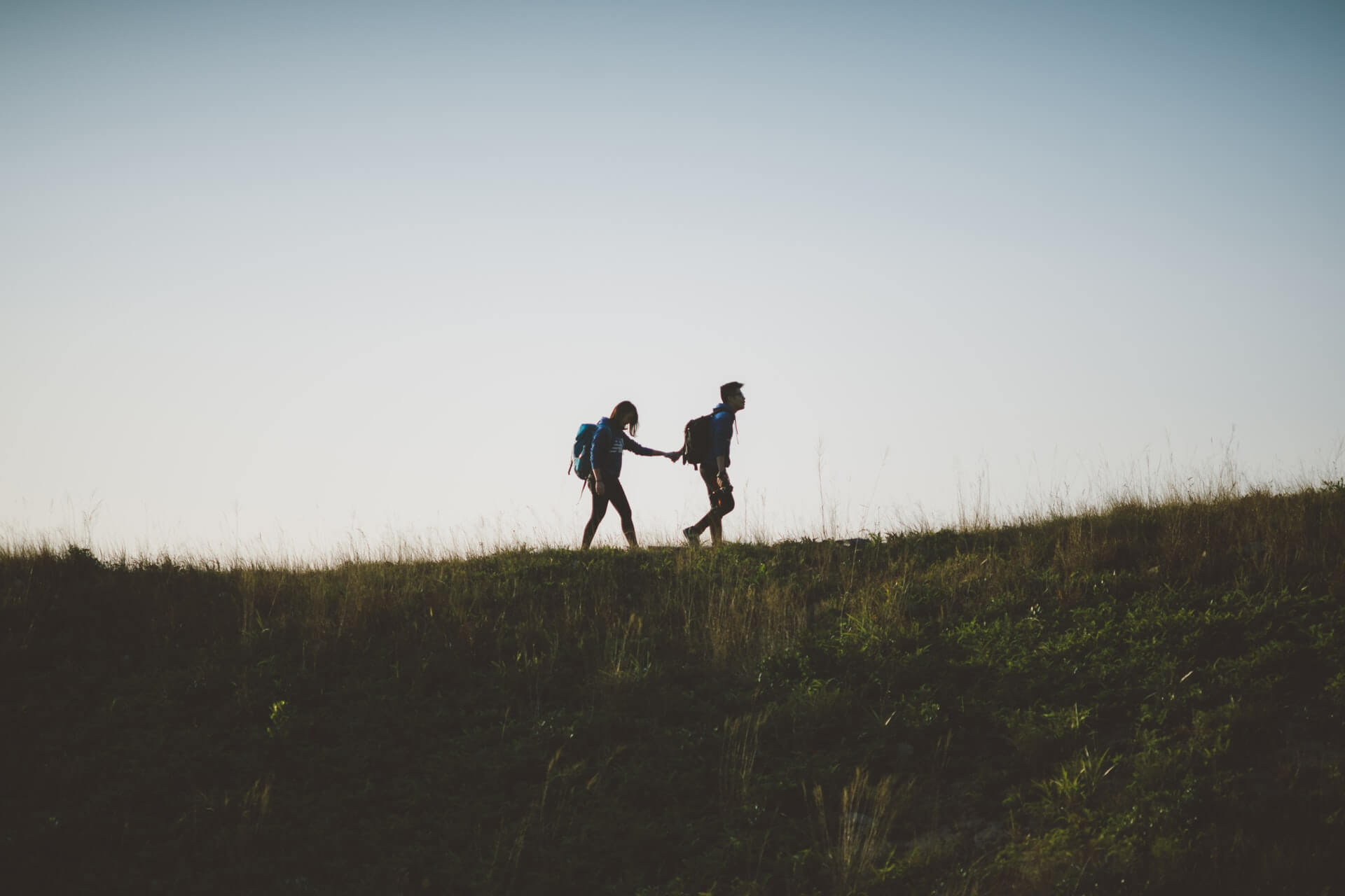 backpacking couple holding hands and walking in a grassy field