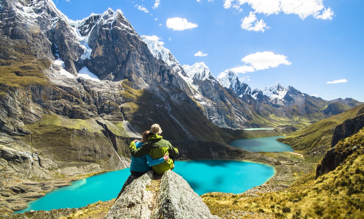 couple sitting on rock staring at a bright blue lake in peru while traveling as a couple