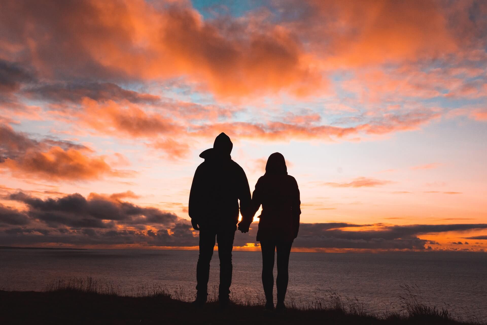 couple holding hands underneath a orange and pink sunset