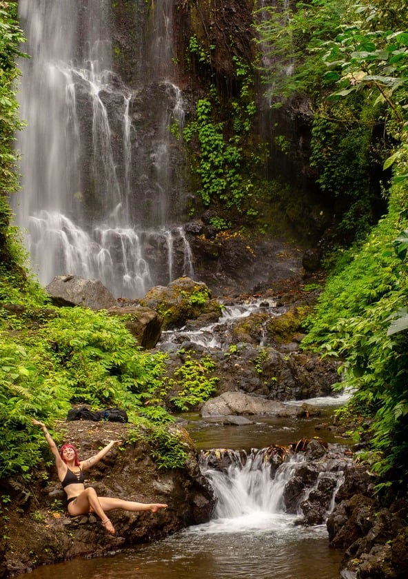 red headed hiker sitting in front of a waterfall in a jungle.
