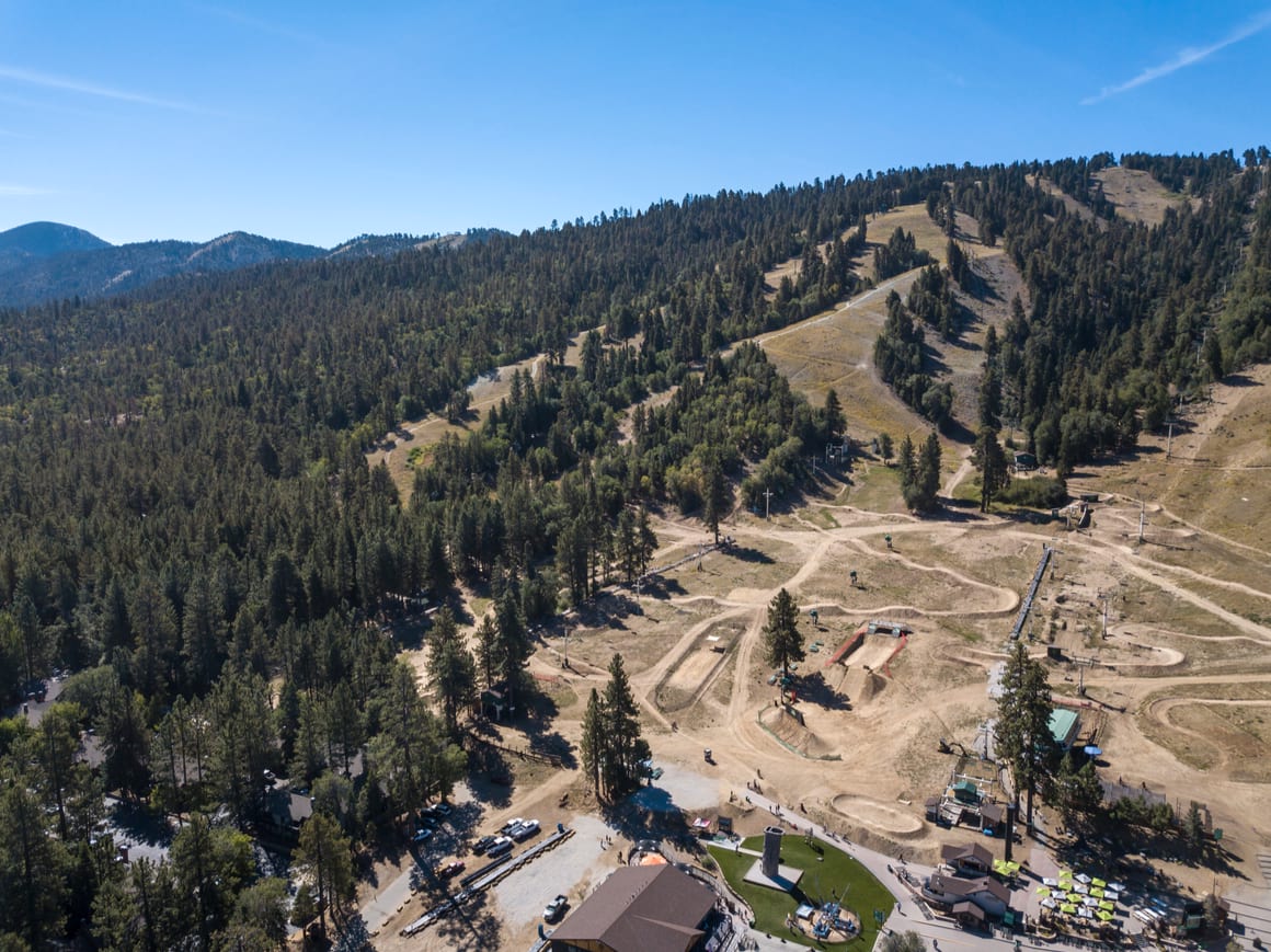 Big Bear Lake East with blue skies showing a resort with a pool and a pine forest from an aerial view