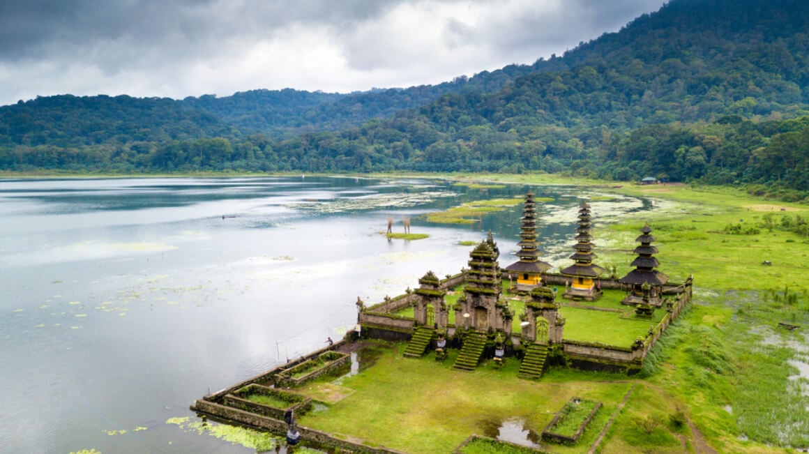 Low aerial view of a Hindu temple by a blue lake.