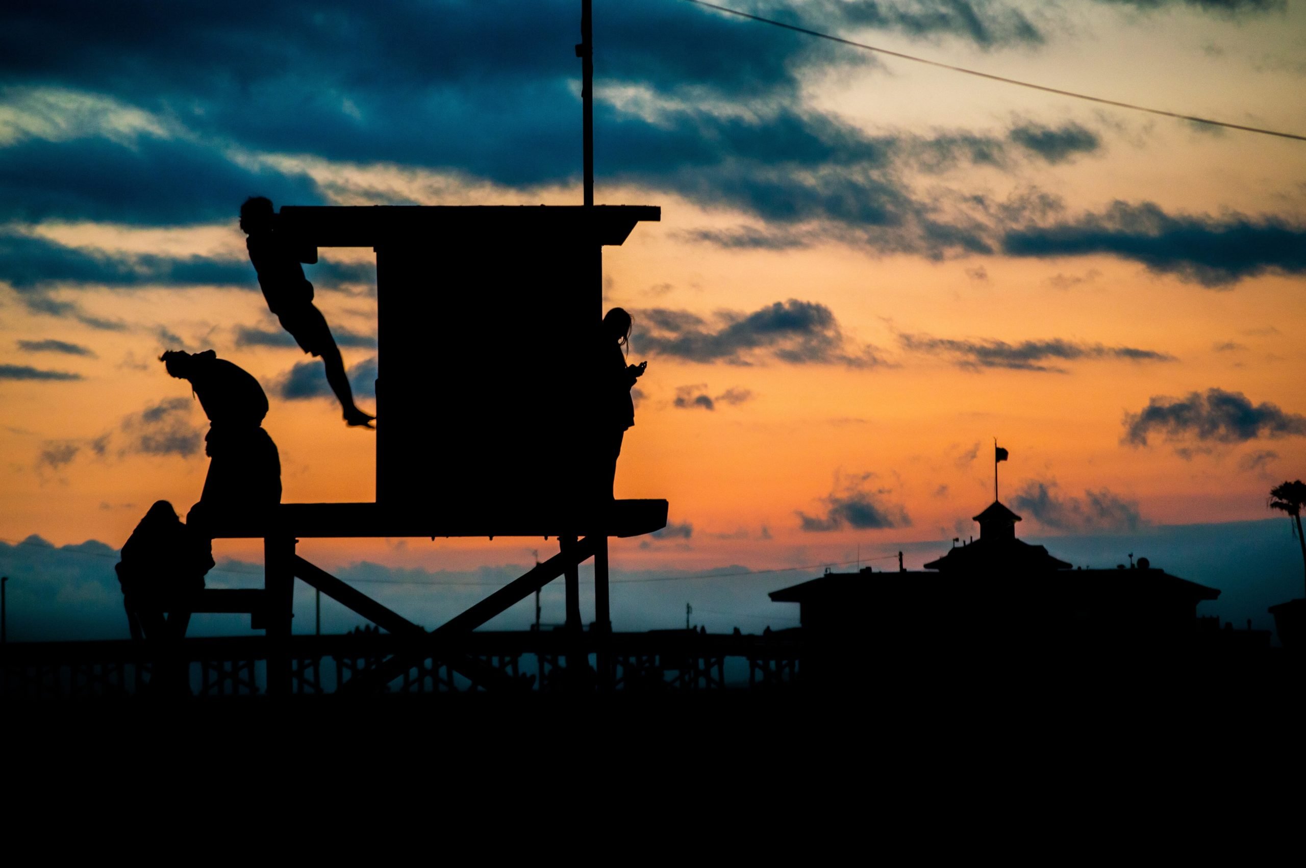 People standing on a lifeguard tower with someone making pull-ups during sunset