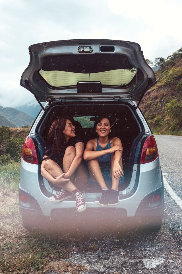 Two girls sit in the trunk of a car.