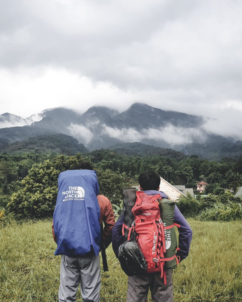 two backpackers standing before an lush green view