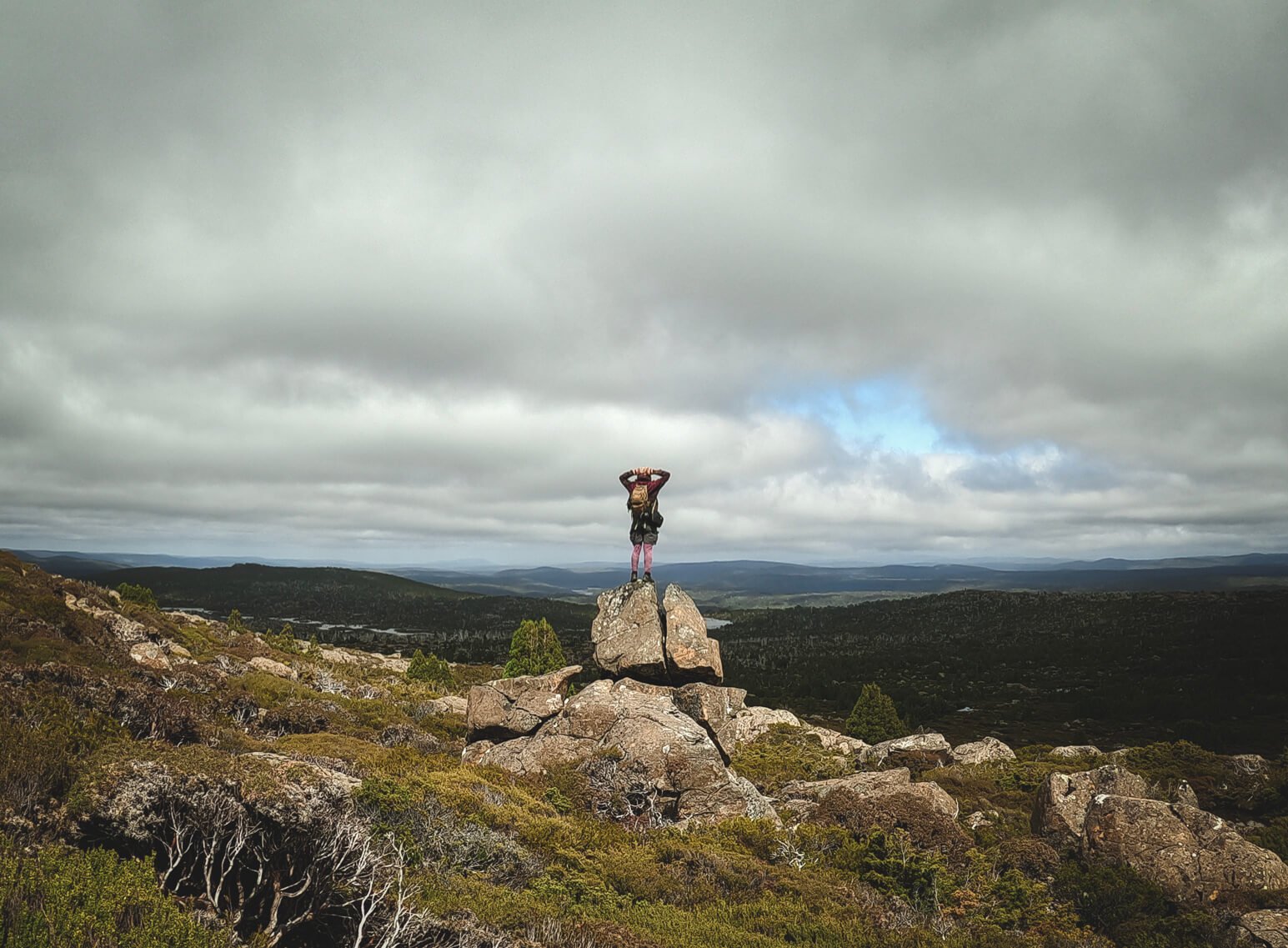 Person stood on top of rock with both hands behind their head overlooking green rolling hills