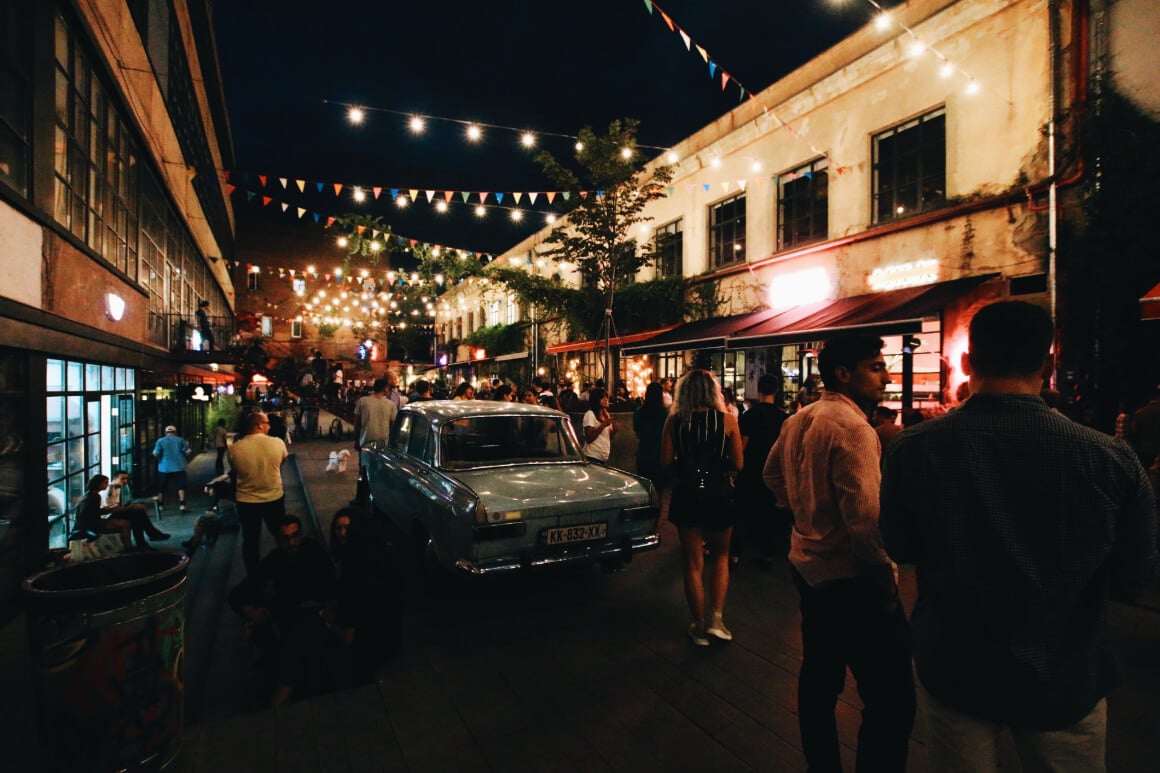 dark courtyard with an old car, peopel and fairy lights